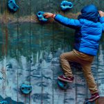 Barn i blå jakke klatrer på klatremur